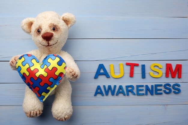 Photo world autism awareness day with teddy bear holding puzzle or jigsaw pattern on heart