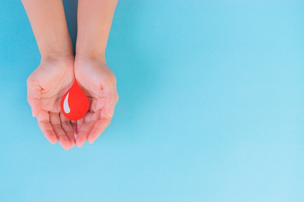 World Blood Donor day, Hemophilia Day concept. Woman hands holding a red blood drop. Copy space.