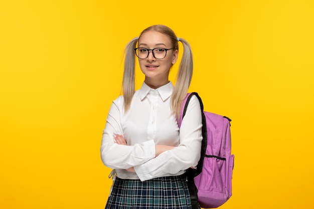 World book day happy blonde girl with crossed hands pink backpack on yellow background