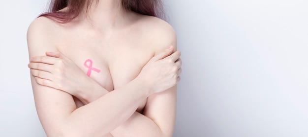 World Breast cancer day concept. Woman covers her chest with her hands with painted pink ribbon. October Breast Cancer Awareness month. Copy space