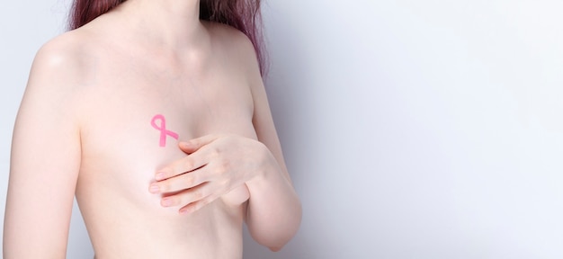 World Breast cancer day concept. Woman covers her chest with her hands with painted pink ribbon. October Breast Cancer Awareness month. Copy space