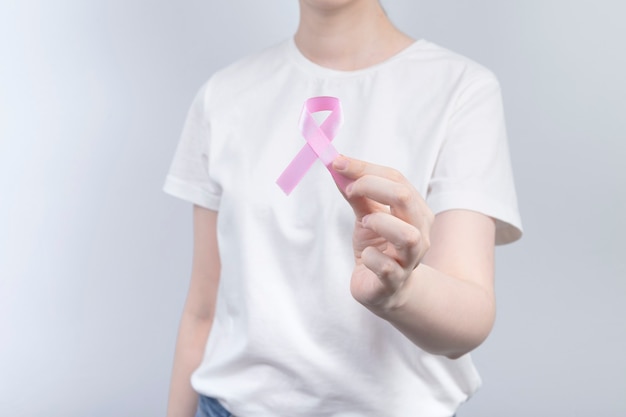 World Breast cancer day concept. Woman in white T-shirt holds pink ribbon in her hand. October Breast Cancer Awareness month