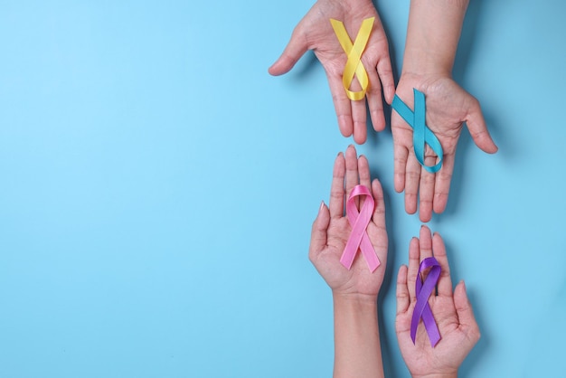 World cancer day. Hands of people holding colorful awareness ribbons for supporting people 