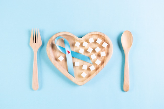 World diabetes day. Blue ribbon with blood drop inside and sugar on plate on pastel blue