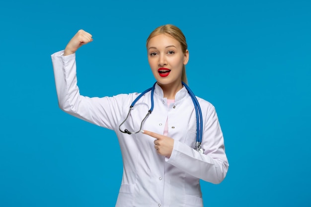 World doctors day strong cute doctor showing biceps with the stethoscope in the medical coat