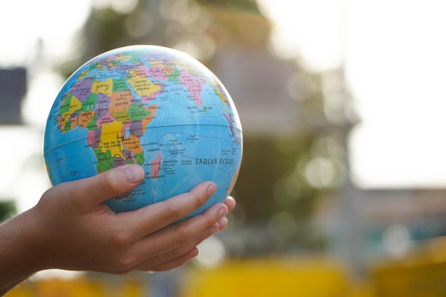 World environment day concept hand of a little girl holding the world blurry green lawn background protect our world copy space