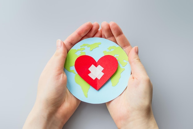 World health day concept Female hands hold a paper model of the globe with a heart