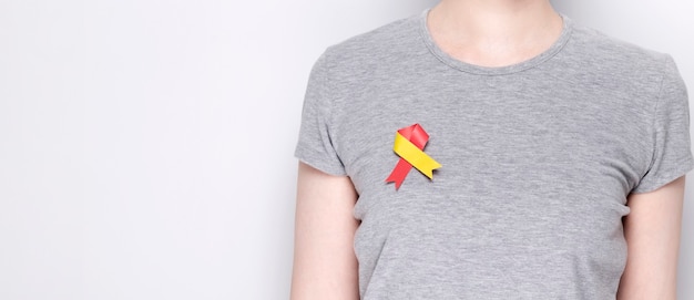 World Hepatitis Day Concept. Girl in gray T-shirt with pinned awareness symbol red-yellow ribbon. Gray background. Copy space