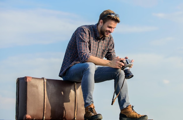 World to see journalist with camera business trip macho man tourist sit on tour bag traveler wait for flight Move sexy man sky background male fashion style looking so trendy