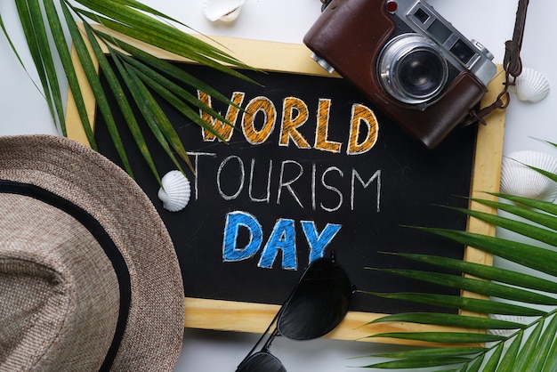 World Tourism Day Typography. Sunglasses, Fedora Hat, Palm Leaf, Camera, Sea Shells and Blackboard