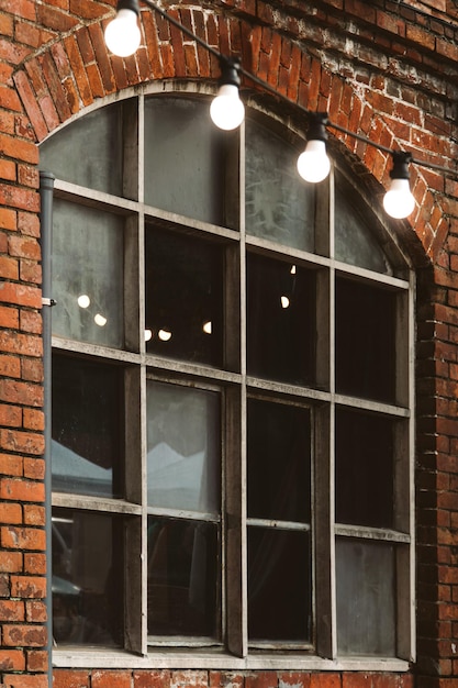 Worn brick wall with a window with industrial glazing and a garland of lighted lights