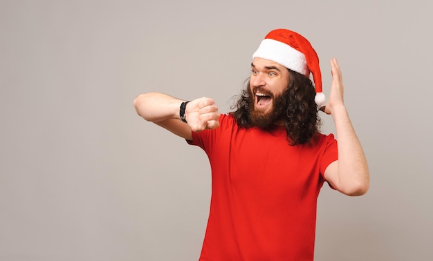 Worried bearded man is looking at the watch and holding hand above head