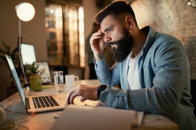 Worried businessman reading an email on a computer while working at night in the office