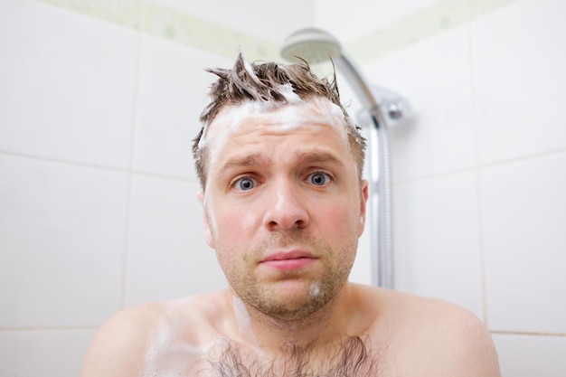 Worried caucasian foamed young man after the water in the shower was turned off looking at the camera