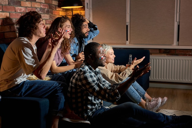 Worried cheering friends or basketball fans watching basketball game on tv at home.Friendship, sports and entertainment concept. Young people worry about favourite team