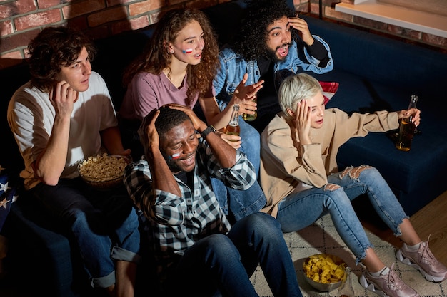 Worried cheering friends or basketball fans watching basketball game on tv at home.Friendship, sports and entertainment concept. Young people worry about favourite team