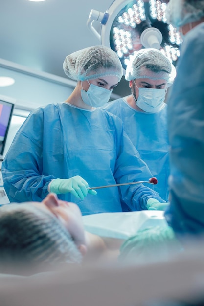 Worried doctor frowning while looking at the stomach of a patient in the surgery theatre. Female medical worker with cotton wool in forceps