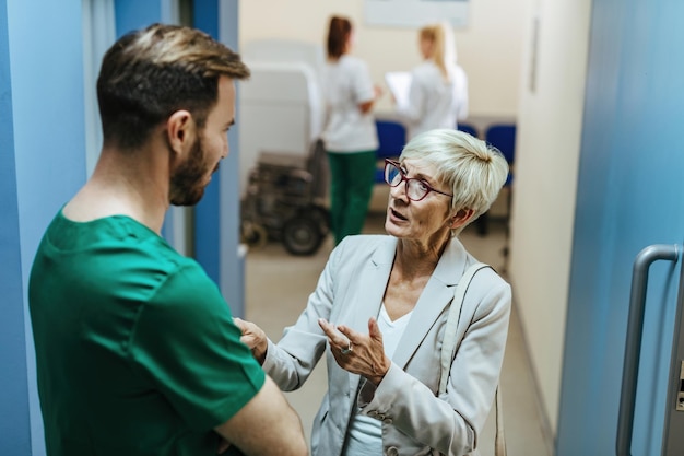 Photo worried mature woman talking to a male surgeon while standing in a lobby at medical clinic