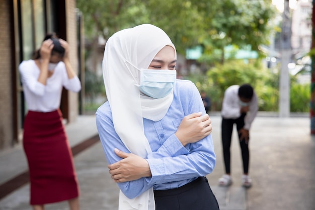 Worried and scared Muslim woman wearing face mask with fear in new normal lifestyle of social distancing keeping distance away from other people in public due to pandemic