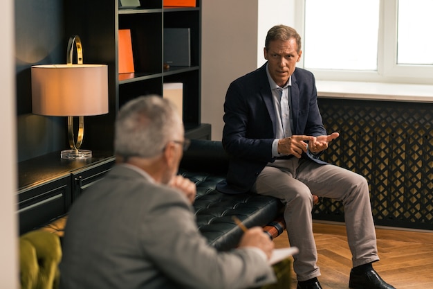 Worried serious man telling about his personal problems to his psychoanalyst in his office