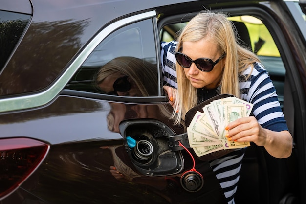 Worried woman with cash in hands looking at the open car tank the concept of rising fuel prices