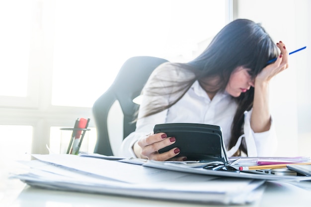 Worried young businesswoman holding calculator over the work desk