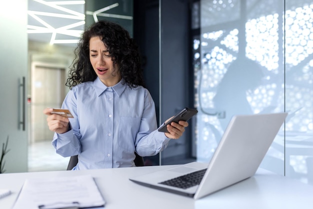 Worried young muslim business woman sitting in the office at the table with a laptop holds the phone