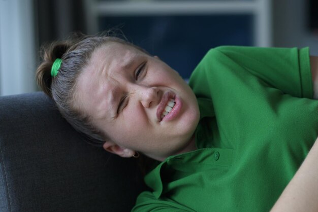 Worried young woman sit on sofa look aside lean forward with folded hands feel fear anxiety teen