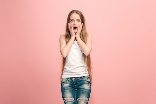 Wow. Beautiful female half-length front portrait on pink  wall. Young emotional surprised teen girl standing with open mouth. Human emotions, facial expression concept. Trendy colors