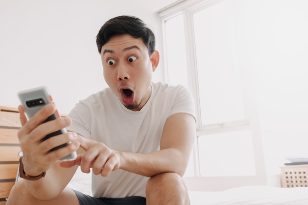 Wow face of man surprised while look at the smartphone in his apartment