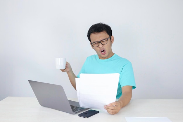 Wow face of Young Asian man shocked what he see in the document when working with laptop isolated grey background wearing blue shirt