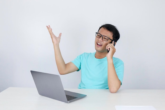 Wow face of Young Asian man shocked what he see in laptop when calling on phone Indonesian man wearing blue shirt