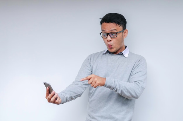 Wow face of Your Asian man shocked what he see in the smartphone on isolated grey background