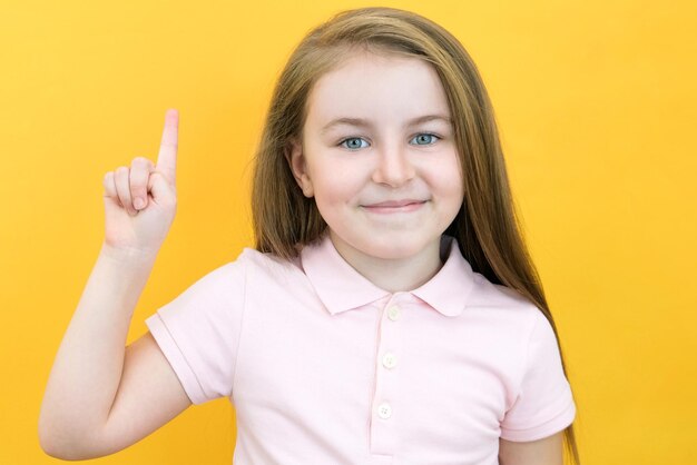 Wow look advertise here Portrait of an astonished cute girl pointing at an empty space in the background a preschooler shows a copy space for an advertisement on a yellow background