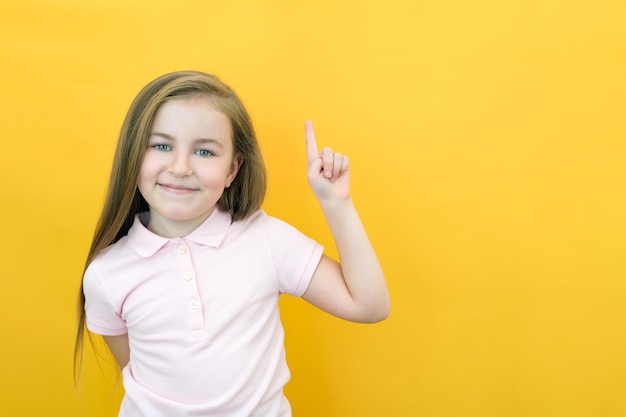 Wow look advertise here Portrait of an astonished cute girl pointing at an empty space in the background a preschooler shows a copy space for an advertisement on a yellow background