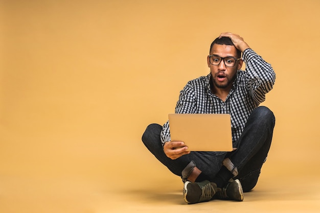 Wow Online working concept African american business man relaxed working and browsing internet on laptop computer Freelancer sitting on floor and typing isolated over beige