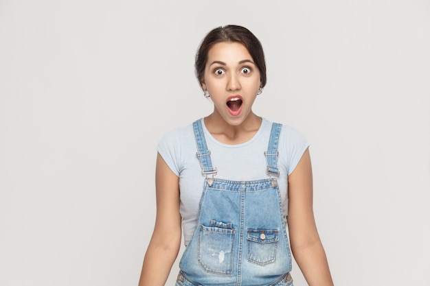 Wow! Portrait of cute woman with shocked facial expression. Studio shot, gray wall