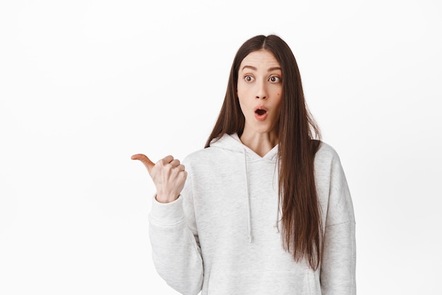 Wow super cool Surprised and thrilled girl gasping fascinated pointing finger aside and looking at awesome promo discount shopping offer standing over white background