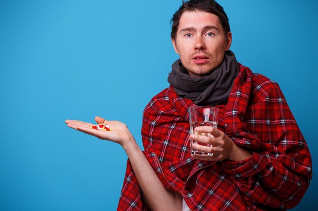 A wrapped in a blanket sick man with tablets and mug in his hands