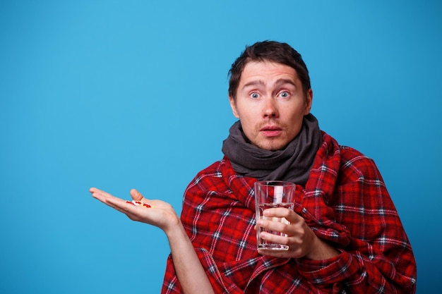 A wrapped in a blanket sick man with tablets and mug in his hands