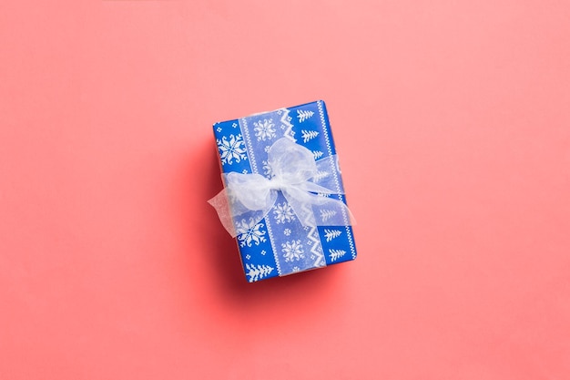 Wrapped Christmas or other holiday handmade present in paper with white ribbon on living coral background. Present box, decoration of gift on colored table, top view with copy space.