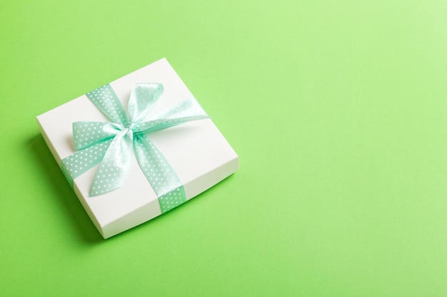 Wrapped Christmas or other holiday handmade present in white paper with green ribbon on colored background Present box decoration of gift on colored table top view with copy space