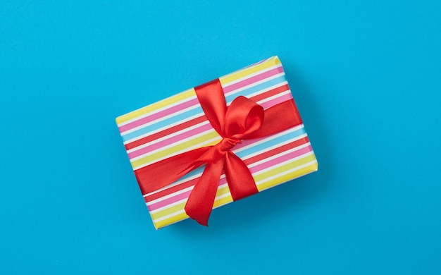 Wrapped gift box with red ribbon bow on blue paper background, top view