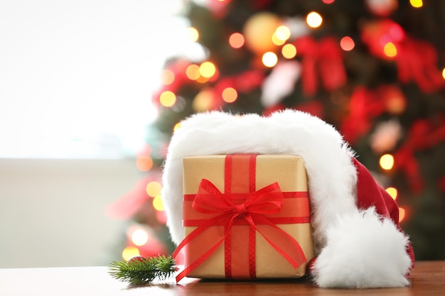 Wrapped gift and Christmas hat on table against blurred festive lights. Boxing day