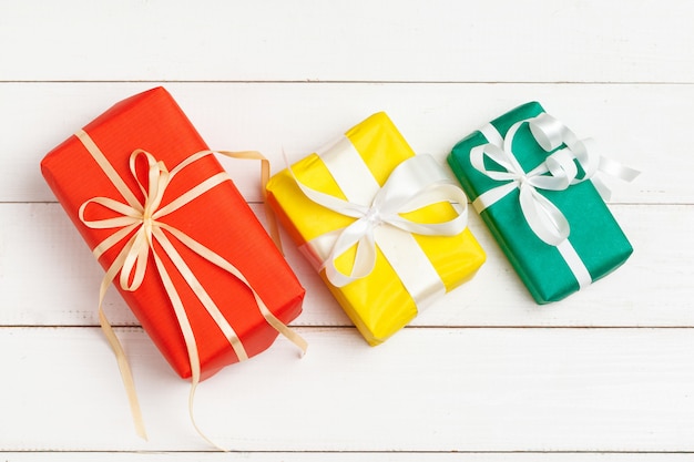 Wrapped gifts with ribbon on white wooden background top view