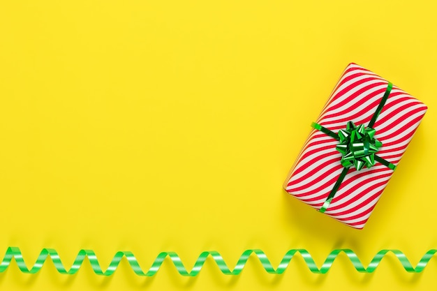 Wrapped present, striped gift box with green bow on yellow paper background.