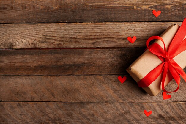 Wrapped vintage gift box with red ribbon bow and hearts on dark wooden table with copy space, greeting card for valentine's day