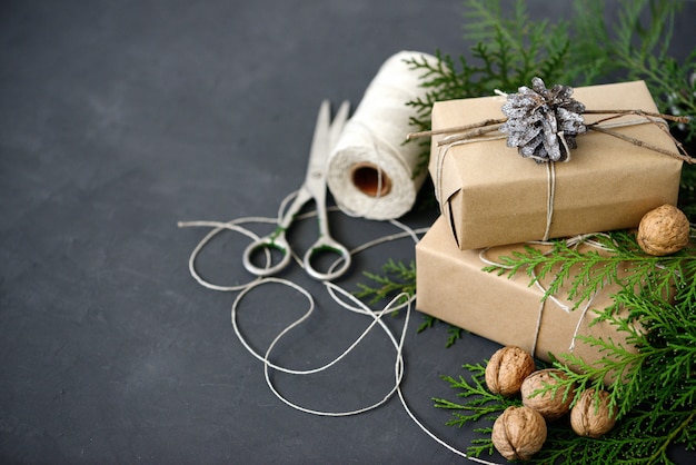 Photo wrapping rustic eco christmas packages with brown paper, string and natural fir branches on dark background