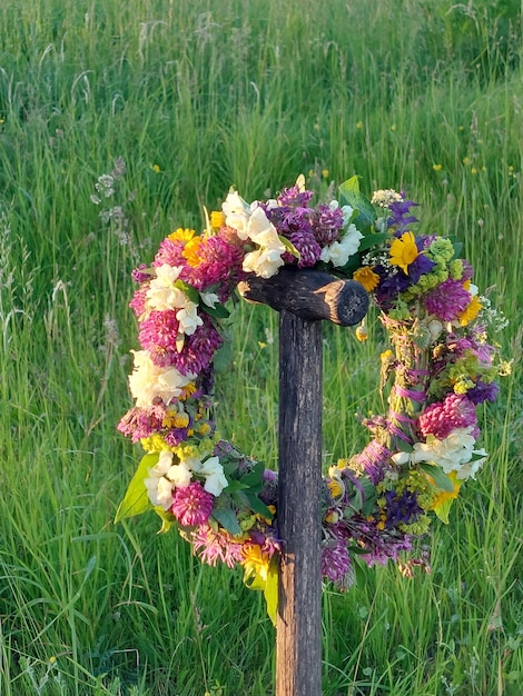 A wreath of meadow flowers on a wooden spade handle on a background of green grass in summer