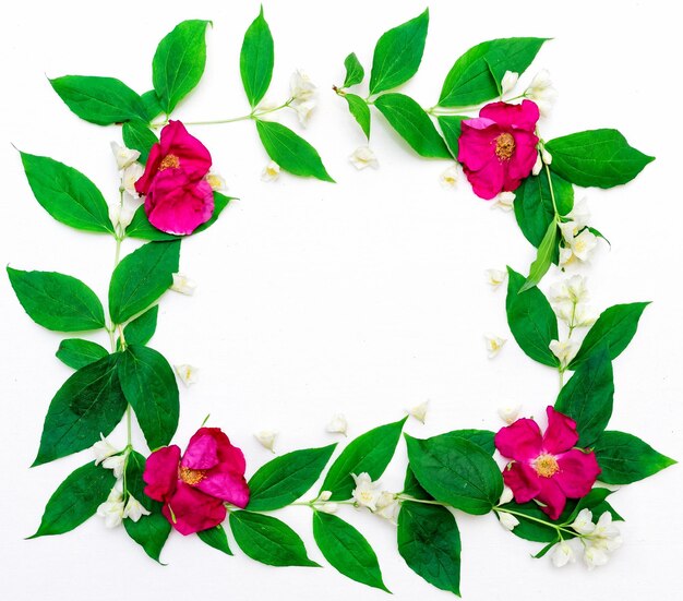 Wreath of pink tea roses and jasmine flowers and leaves on white background. Flat lay.